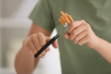 Stop smoking concept. Woman cutting cigarettes on light background, closeup