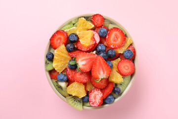 Yummy fruit salad in bowl on pink background, top view