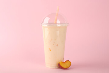 Plastic cup of tasty smoothie and fresh peach on pink background