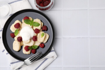 Plate of tasty lazy dumplings with raspberries, sour cream and mint leaves on white tiled table,...