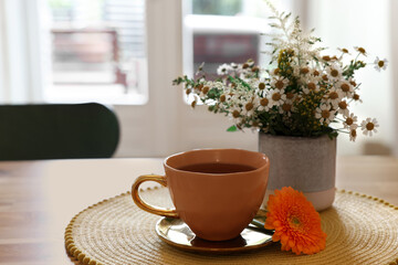 Cup of delicious chamomile tea and fresh flowers on table in room. Space for text