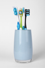 Different toothbrushes in holder on light grey background