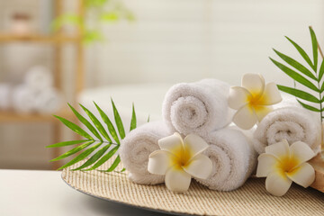 Fototapeta na wymiar Spa composition. Towels, plumeria flowers and palm leaves on white table in bathroom