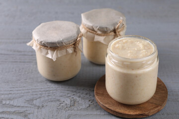 Spicy horseradish sauce in jars on grey wooden table, closeup