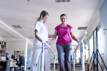 The physiotherapist and her patient are doing rehabilitation on the parallel bars in the gym.