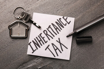Inheritance Tax. Paper note, key with key chain in shape of house and marker on grey table, flat lay