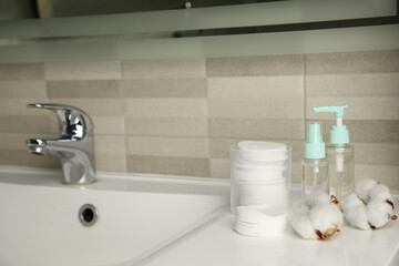 Cotton pads, cosmetic products and flowers on sink in bathroom