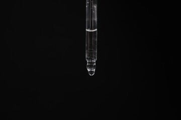 Dripping cosmetic serum from pipette against black background