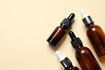 Many bottles with face serums on beige background, flat lay. Space for text