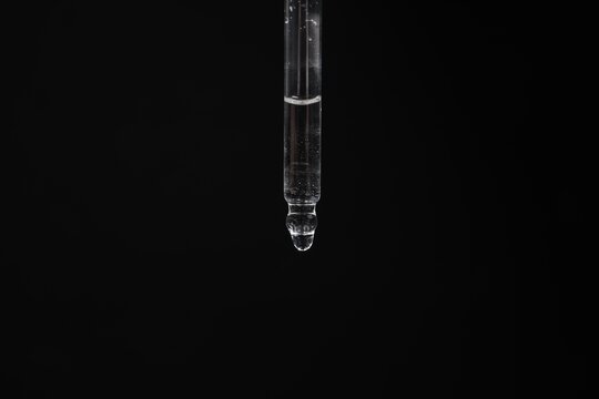 Dripping cosmetic serum from pipette against black background