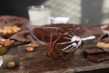 Whisk with chocolate cream on table, closeup. Space for text