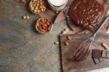 Bowl of chocolate cream, whisk and ingredients on textured table, flat lay. Space for text