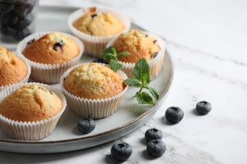 Delicious sweet muffins with blueberries and mint on white marble table, closeup. Space for text