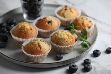 Delicious sweet muffins with blueberries and mint on white marble table, closeup