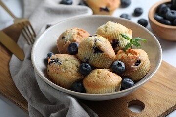 Delicious muffins with blueberries and mint in bowl on table, closeup