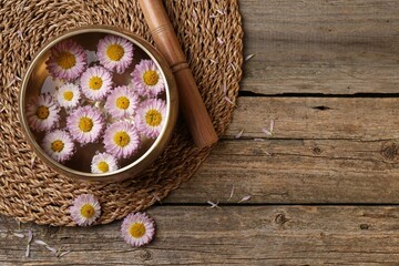 Tibetan singing bowl with water, chrysanthemum flowers and mallet on wooden table, flat lay. Space...