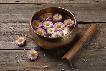 Tibetan singing bowl with water, chrysanthemum flowers and mallet on wooden table