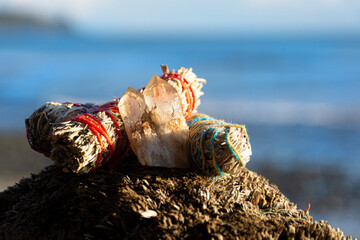 An image of three colorful white sage smudge sticks and healing crystal resting on driftwood with...
