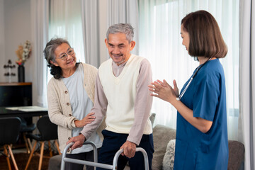 an elderly man patient being assist by home health nurse,using walker to walk at home,a senior female wife standing and supporting beside him,concept of homecare,home health nursing