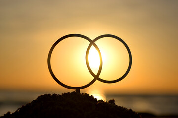 Black outlines of wedding rings at dawn and sunset on seashore. Stick contours in shape of wedding...