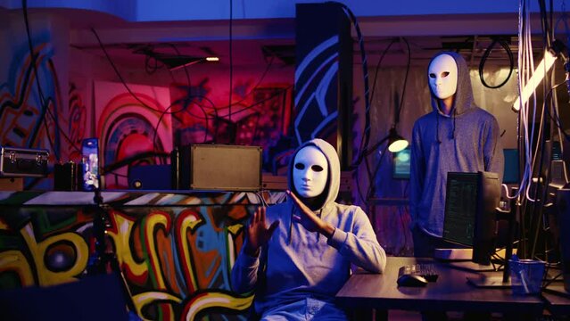 Hacker group members doing online terrorism acts, filming ransom video with smartphone in hidden underground base, threatening to release stolen sensitive data publicly if payout demands are not met