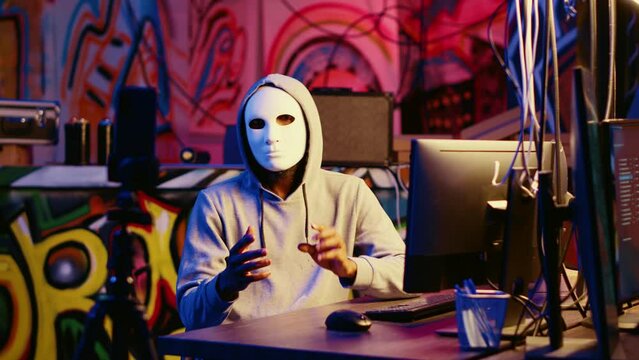 Anonymous masked dissident hacker filming anti government message, fighting against propaganda. Hooded social justice crusader using smartphone to record threatening video