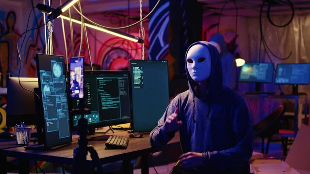 Masked hackers filming video threatening to not stop coordinating DDoS attack on website and send large amounts of traffic from multiple sources to overwhelm it unless their demands are not met