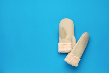 Warm women's beige mittens on blue. Space for text.