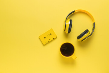 Monochrome image of a yellow coffee cup, cassette tape and headphones on yellow. Space for text. - obrazy, fototapety, plakaty