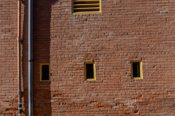 red brick wall with small yellow windows and vent, with copy space