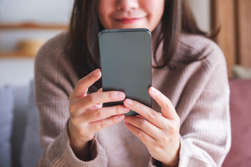 Closeup image of a young woman holding and using smart phone at home