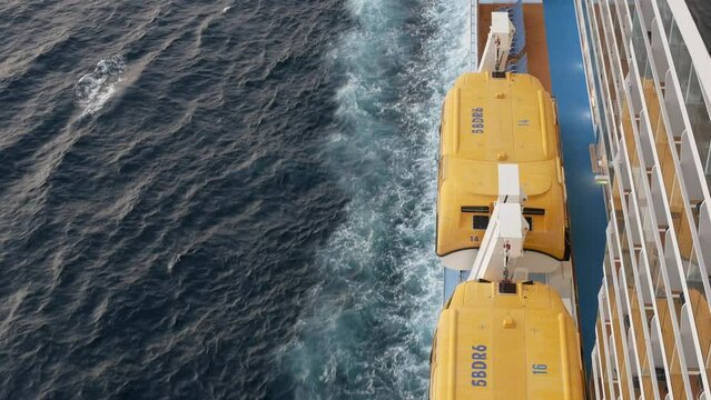 Lifeboat on giant cruise ship view down to ocean surface with waves tail below while ship cruising saling in the sea. Safty muster lifeboat equipment.