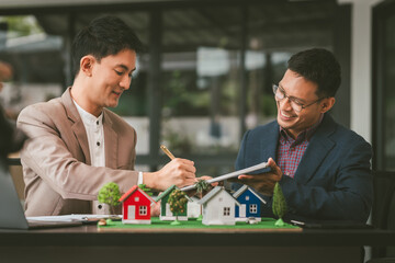 Two professionals smiling, discussing over model houses on a table, possibly planning or reviewing...