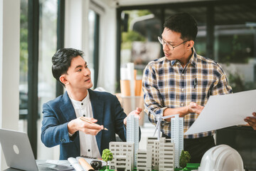 Two middle-aged Asian people businessmen, one holding wind turbine model, discussing over model...