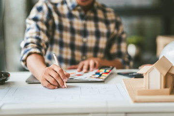 Asian businessman person with glasses examining architectural blueprints next to model house,...