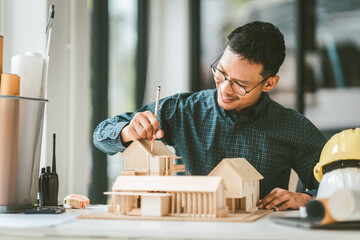 Asian businessman person with glasses examining architectural blueprints next to model house,...
