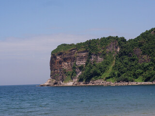 Fototapeta na wymiar Concrete pier on a rocky island cliff facing the calm ocean on a clear sunny day.