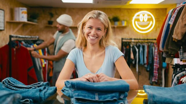 Portrait of smiling female sales assistant sorting stock of denim jeans in pop up fashion or clothes store - shot in slow motion