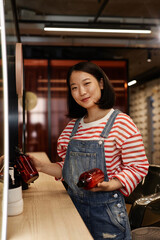 Vertical waist up portrait of young Asian woman as hairstylist in beauty salon smiling at camera...