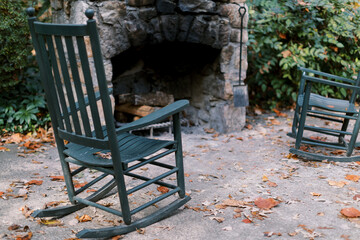 Fototapeta na wymiar Green rocking chairs in front of an outdoor stone fireplace and patio, a cozy and serene retreat amid fall foliage.