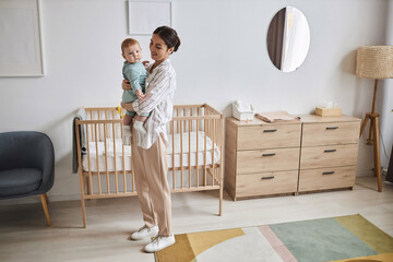 Full length portrait of smiling young mother holding baby boy in minimal room interior, copy space