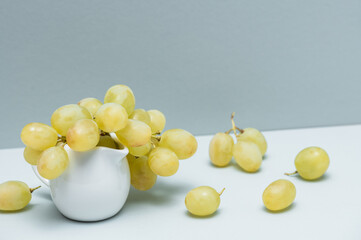 Grapes in a white jug on a gray background.