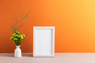 A bouquet of small green chrysanthemums in a white vase and a photo frame on an orange background.
