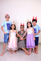 Senior grandmother sitting on the sofa surrounded by her loving grandchildren to celebrate Christmas