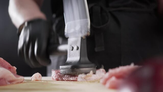 The chef turns over a pork chop and quickly beats a meat hammer on a wooden board.