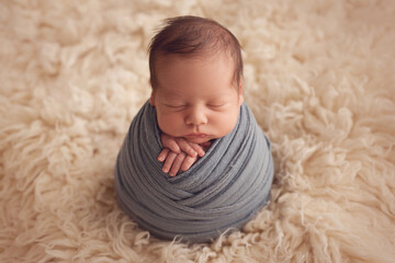 Newborn baby boy sleeps wrapped in a cocoon on white fur