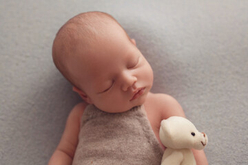 Newborn baby boy sleeps in a beige suit and hugs a toy bear