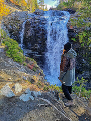 A girl on the background of a beautiful waterfall in the autumn mountains beyond the Arctic Circle...