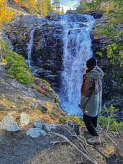 A girl on the background of a beautiful waterfall in the autumn mountains beyond the Arctic Circle...