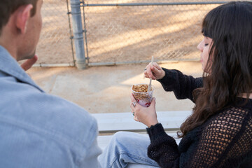 Couple eats yogurt and protein bar on bleachers outside